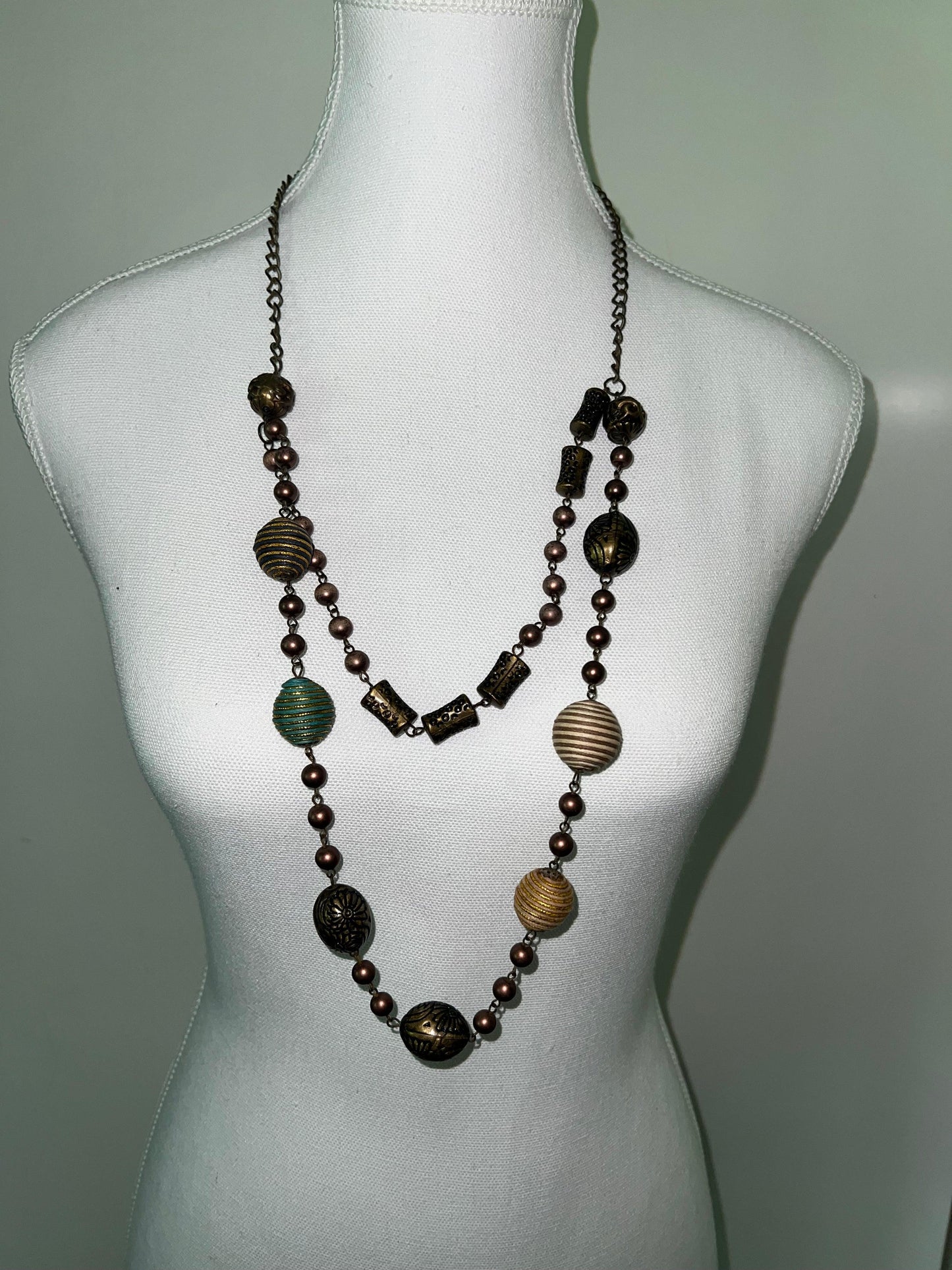 Vintage beaded necklace with unique bronze, gold, and teal beads in various sizes and textures on a white mannequin.
