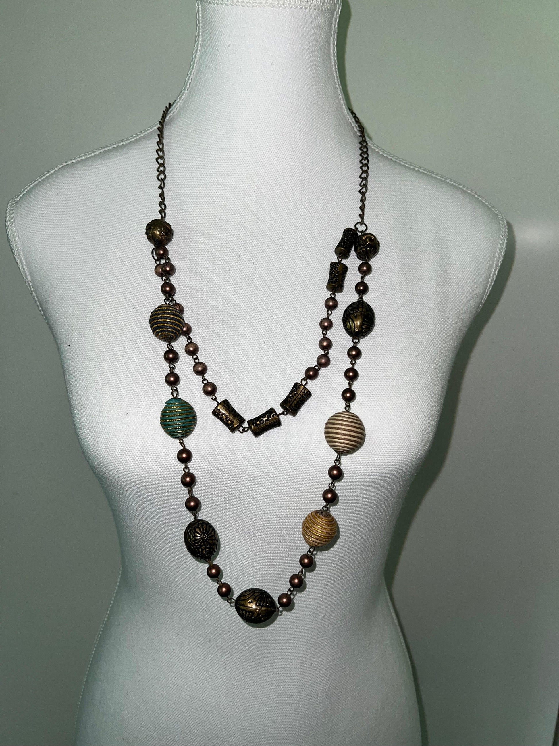 Vintage beaded necklace with unique bronze, gold, and teal beads in various sizes and textures on a white mannequin.