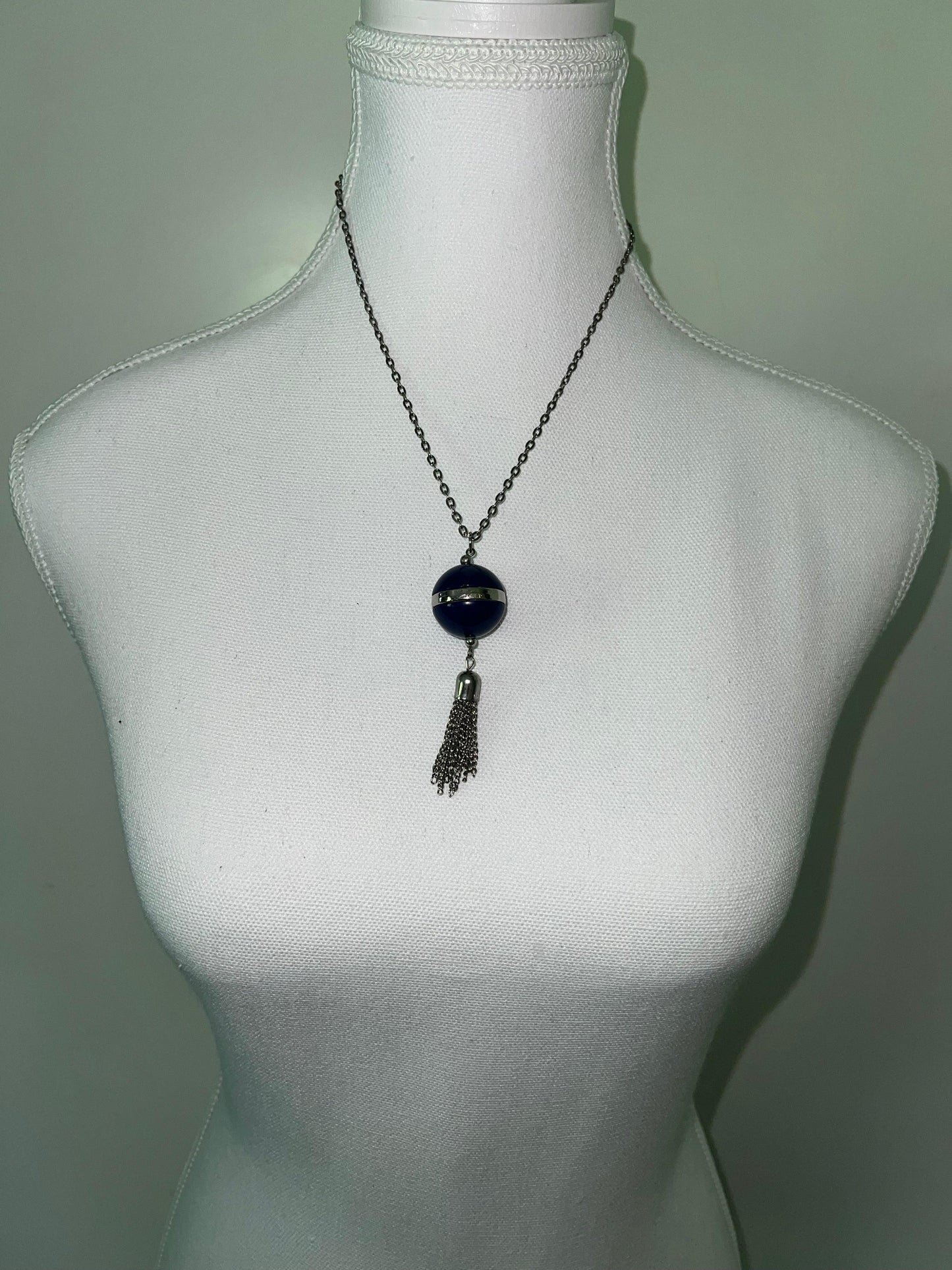Blue orb pendant necklace with silver chain and tassel, displayed on a white mannequin.