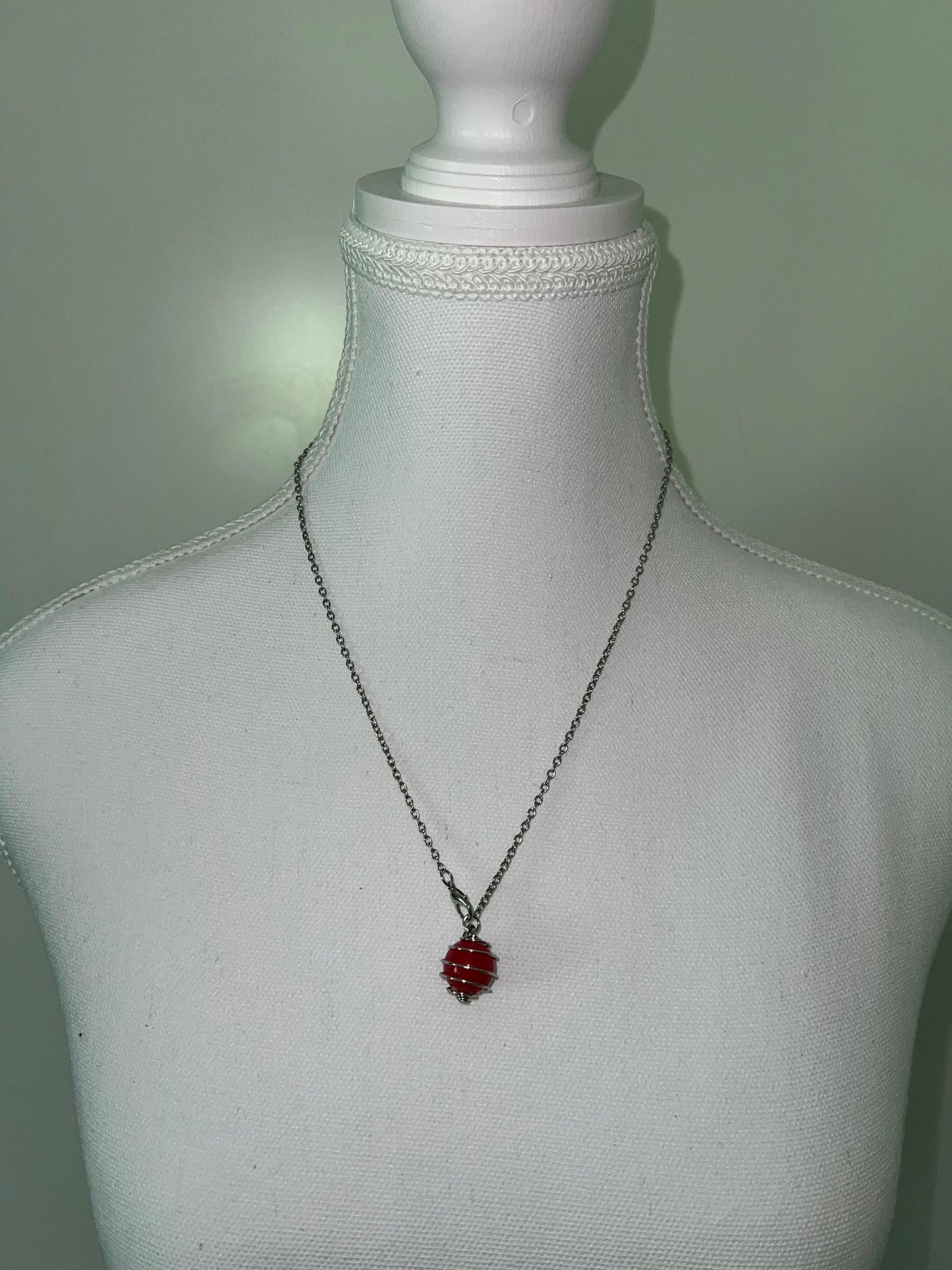 Silver spiral necklace with a striking red accent bead, displayed on a white mannequin.