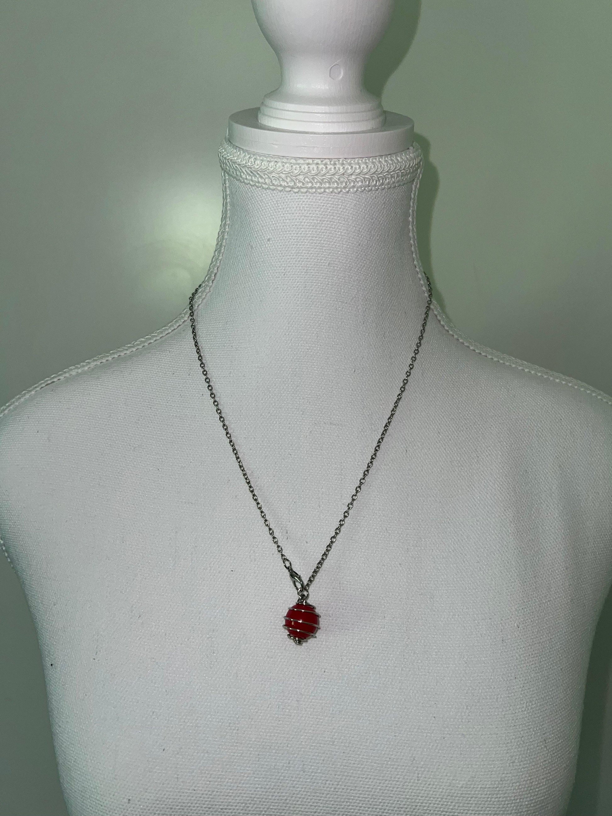 Silver spiral necklace with a striking red accent bead, displayed on a white mannequin.