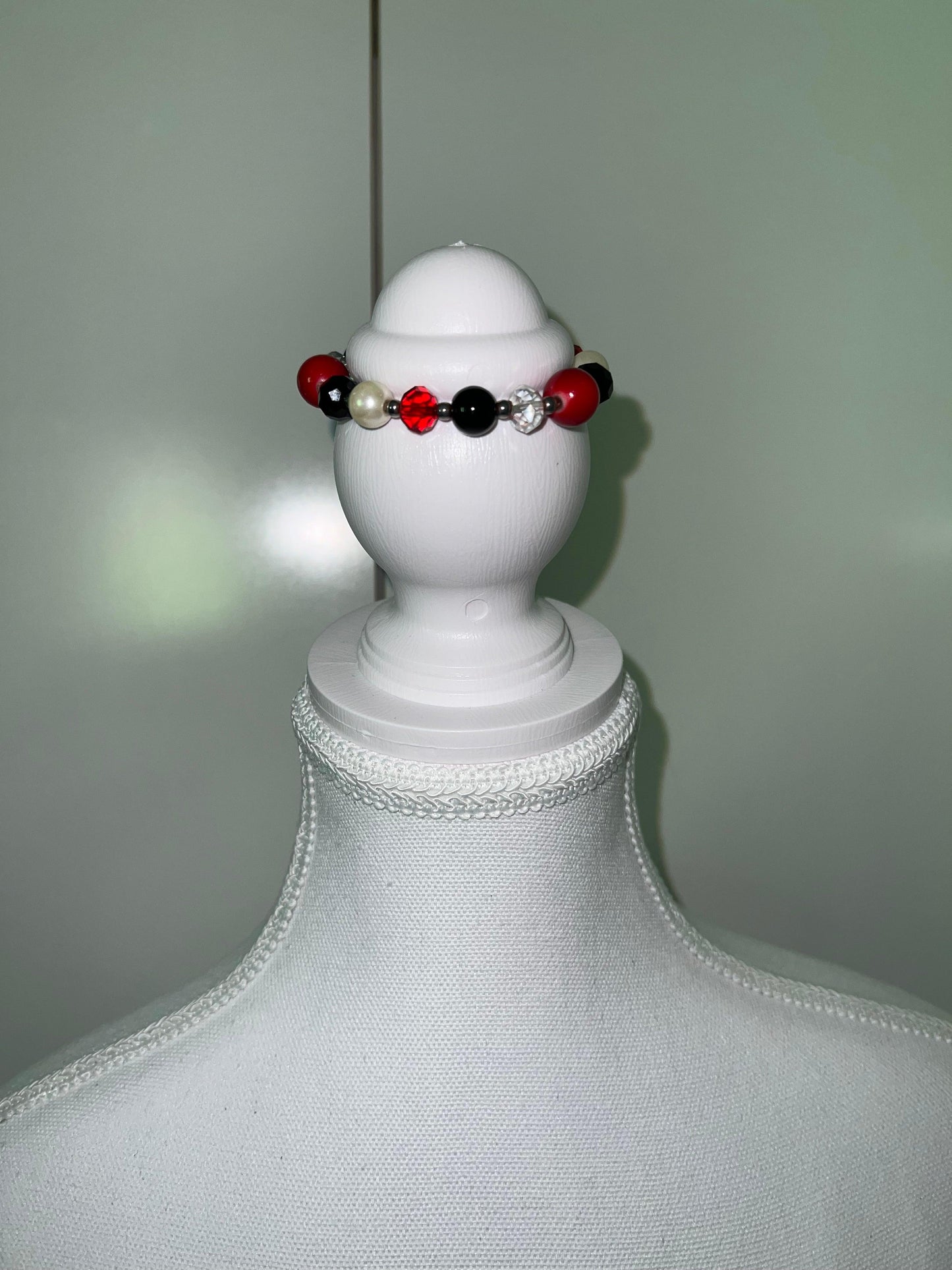 Red, black, and pearl beaded bracelet with a clear rhinestone bead on a white jewelry display.