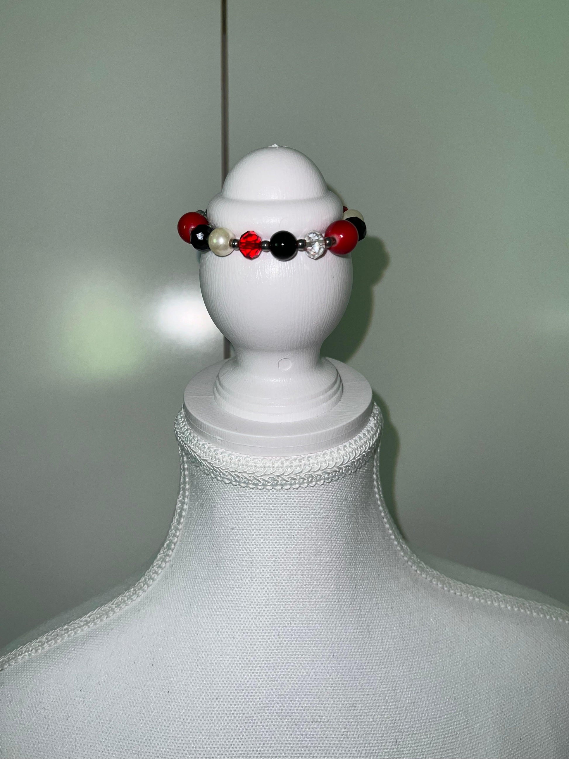 Red, black, and pearl beaded bracelet with a clear rhinestone bead on a white jewelry display.